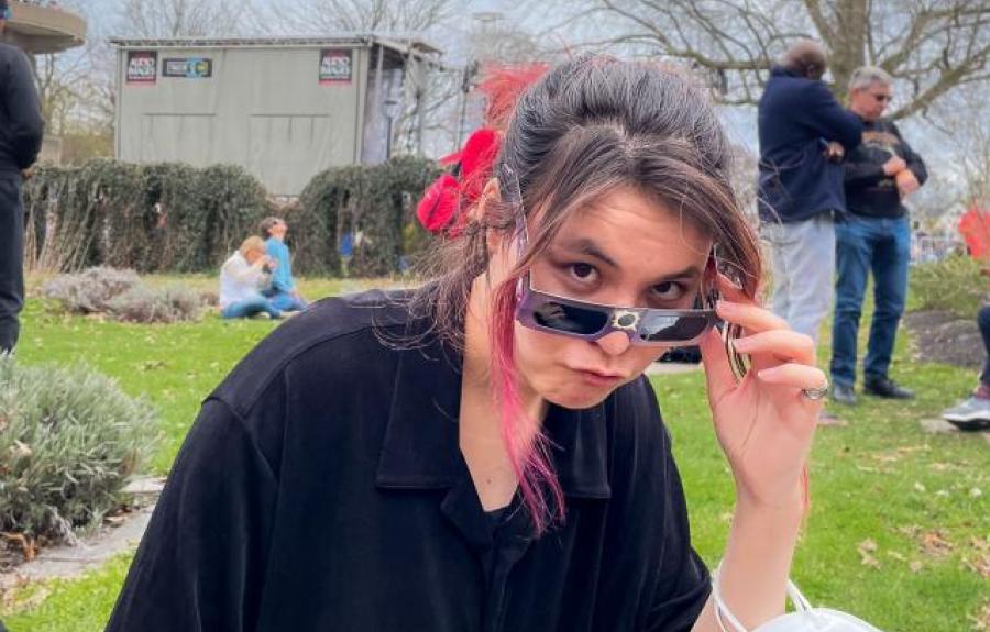 Asian women peeking over sunglasses in outdoor garden setting.
